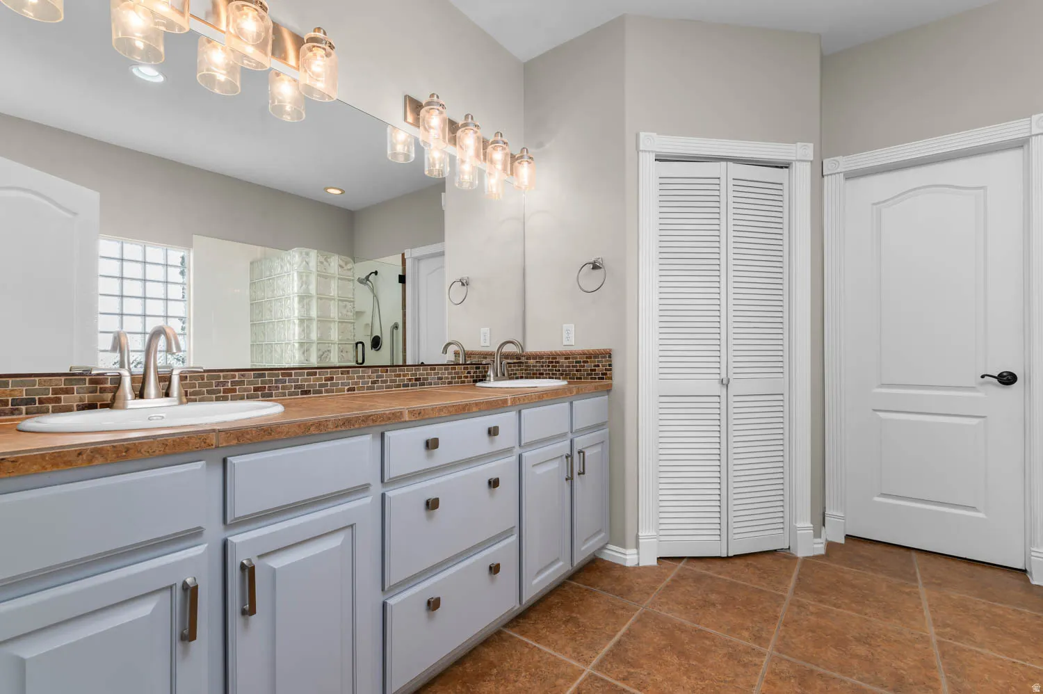 Dual vanity with integrated sinks and brushed nickel faucets, set against a mosaic tile backsplash