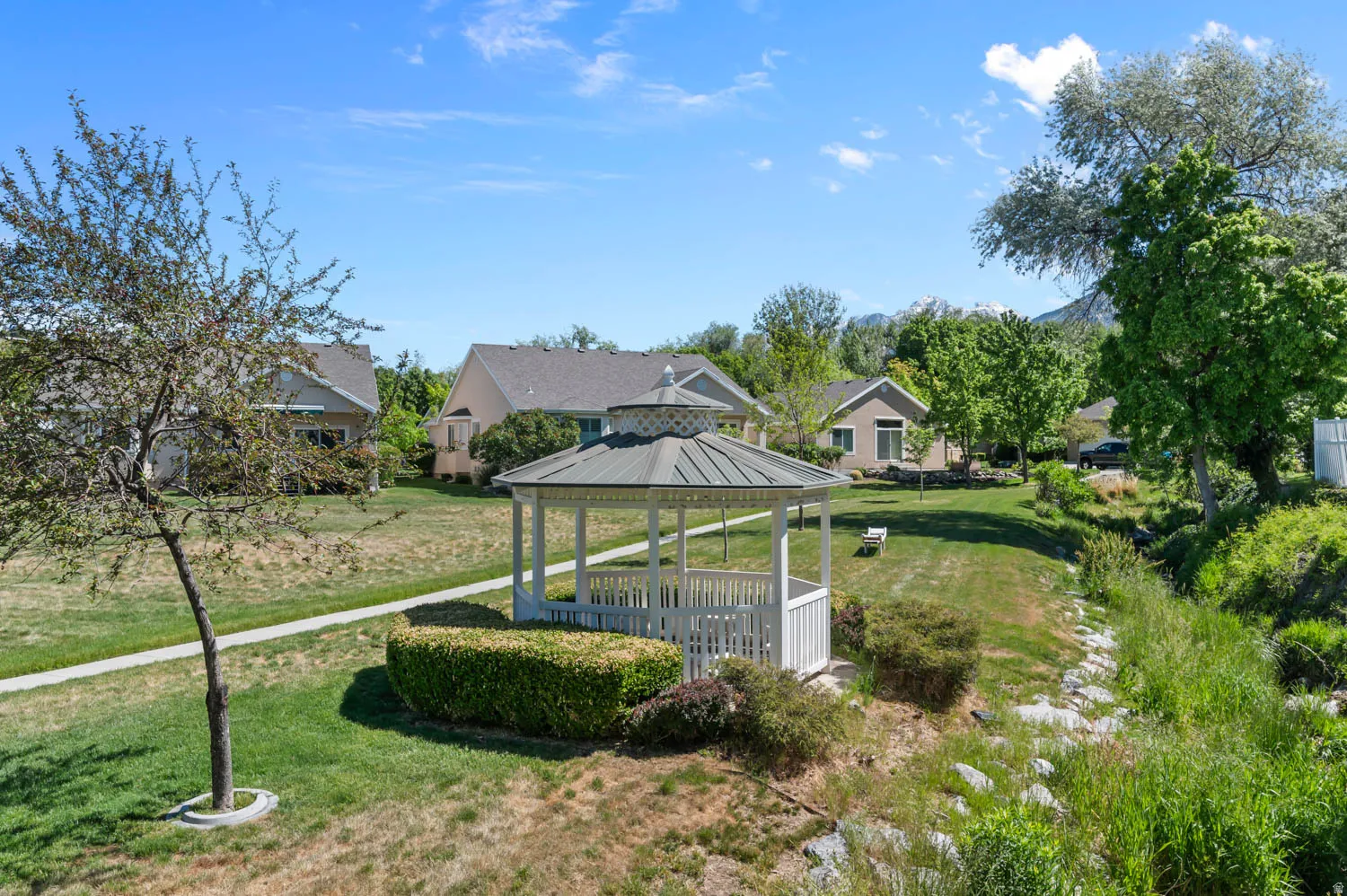 White gazebo with a multi-tiered roof, surrounded by green lawns and mature trees
