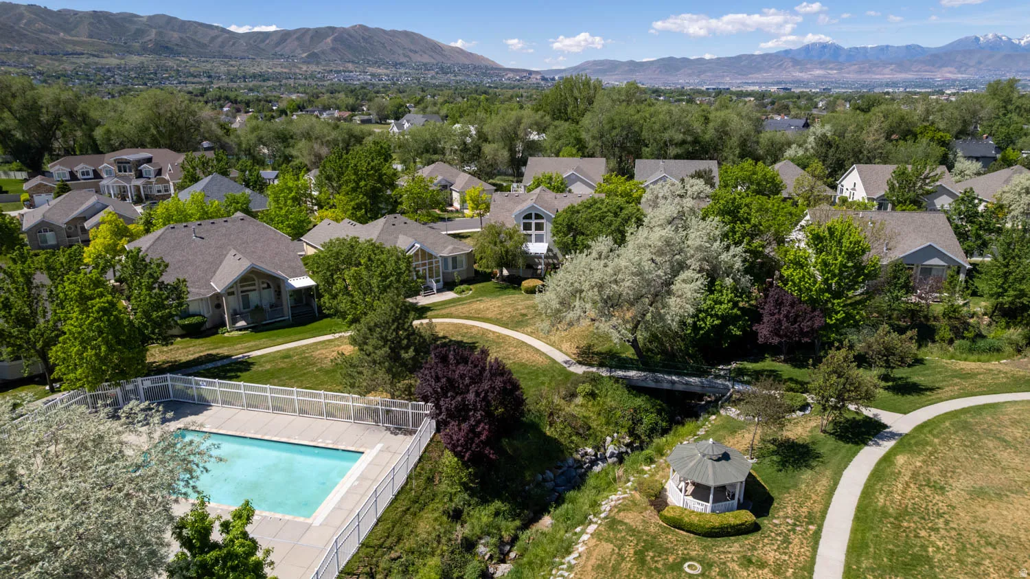 Community amenities featuring a fenced swimming pool, winding paved pathways, a decorative gazebo, and a footbridge over a stream