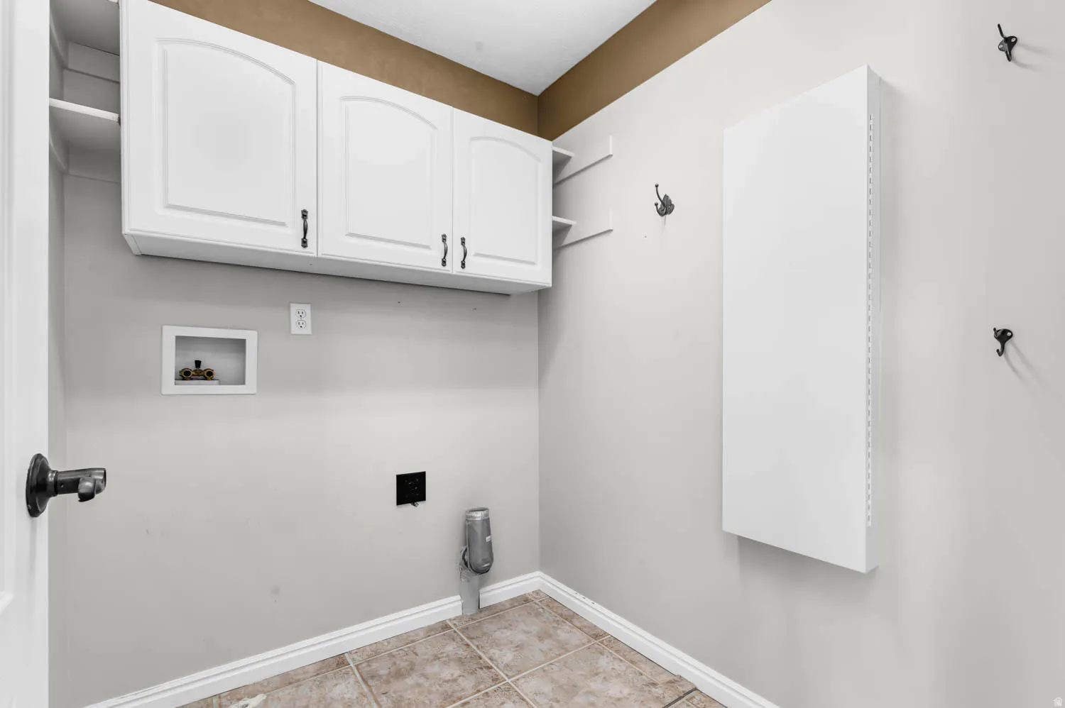 Utility room featuring overhead white cabinetry with arch panel doors and dark hardware, open shelving, and tiled flooring