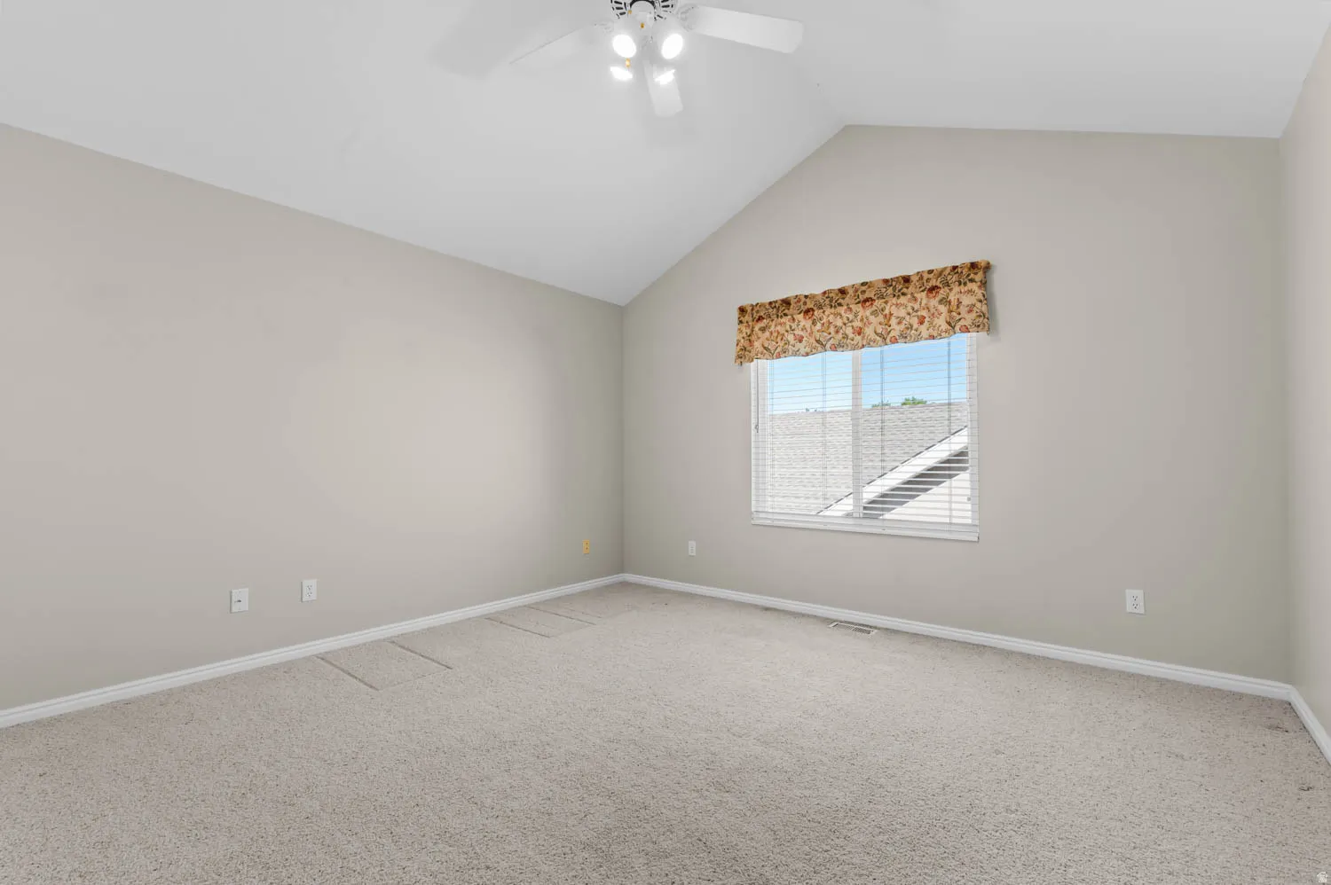 Carpeted room featuring a vaulted ceiling with a ceiling fan, a window with horizontal blinds, and neutral-toned walls