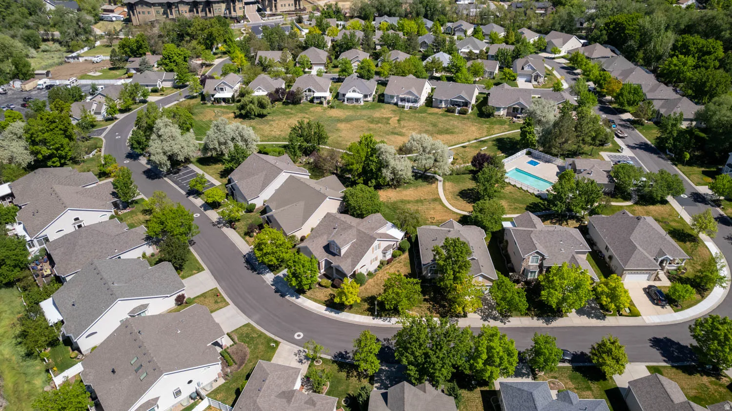 Aerial perspective of a residential community featuring curvilinear streets, varied rooflines, and mature green landscaping