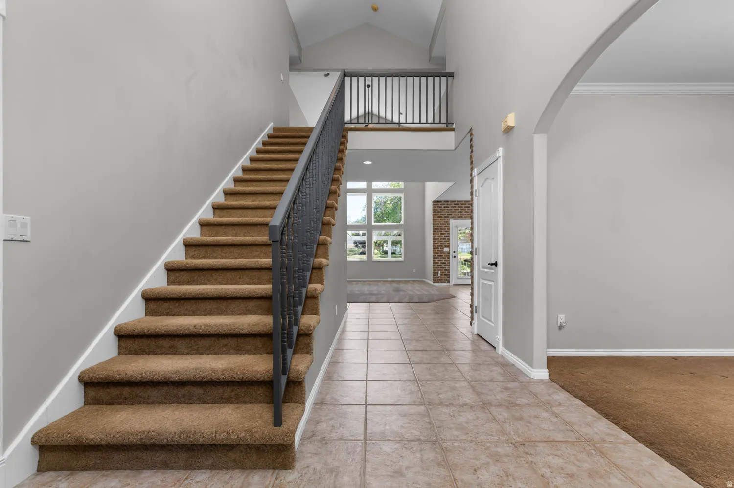 Two-story entryway featuring a carpeted staircase with dark iron balusters, tiled flooring, vaulted ceilings, and an arched doorway