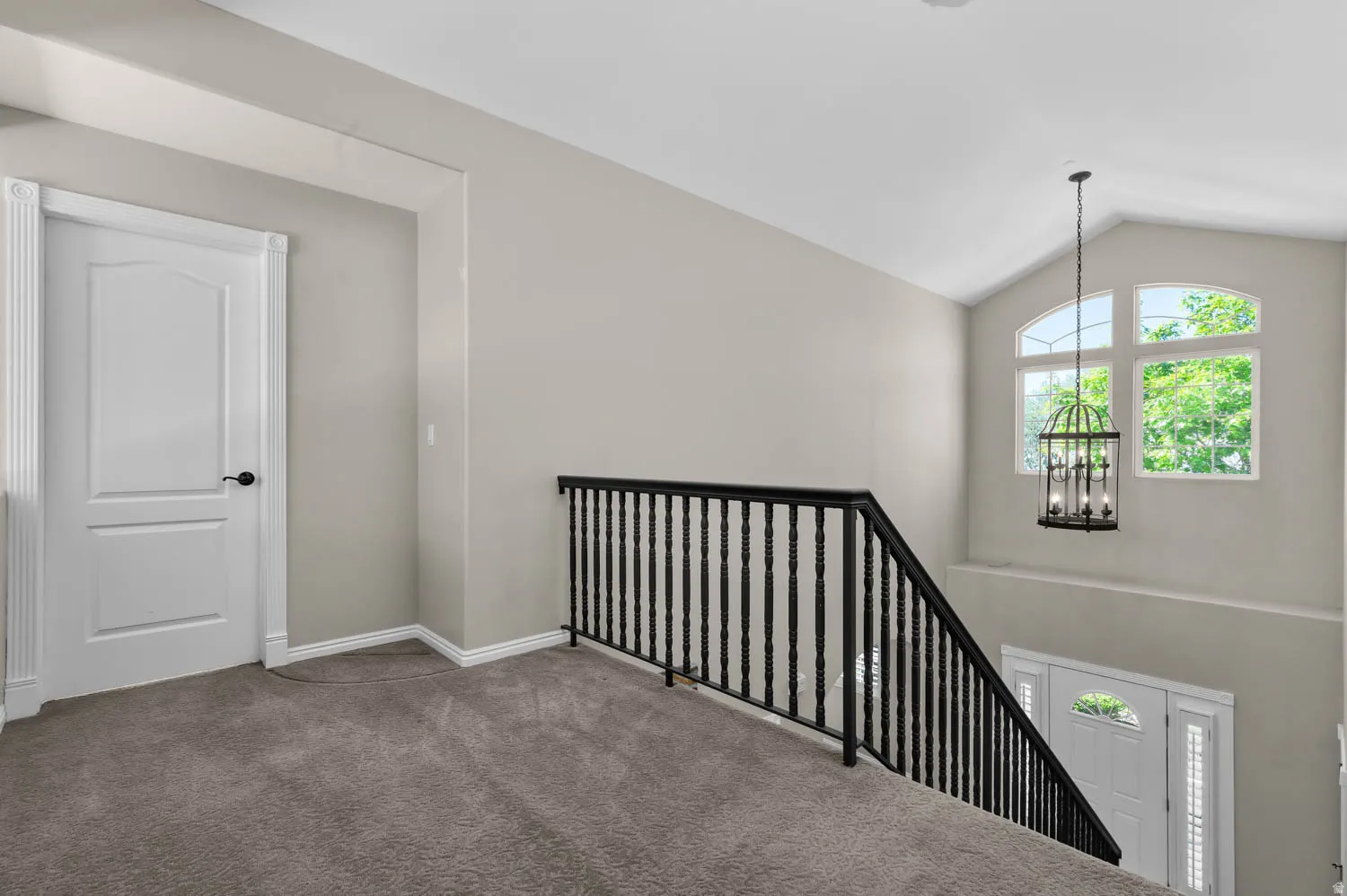 Upper-level hallway featuring plush gray carpeting, a white paneled door with black hardware, and a black wrought iron staircase railing
