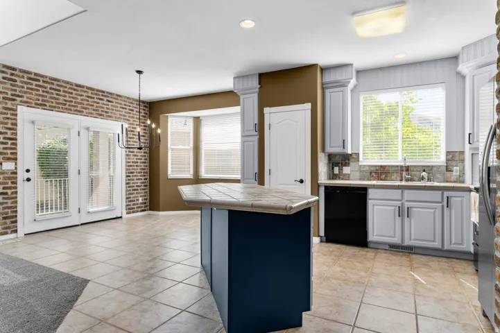 Kitchen featuring an island with a tiled countertop, light cabinetry, and black appliances
