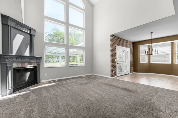 Vaulted ceiling living area featuring a fireplace with decorative mantel, expansive picture windows, and gray patterned carpeting