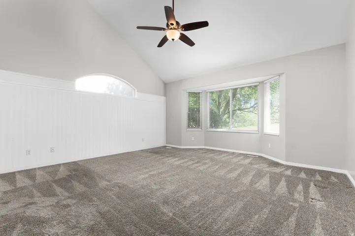 Spacious room with a vaulted ceiling, a multi-panel bay window, a semi-circular transom window, and white wainscoting