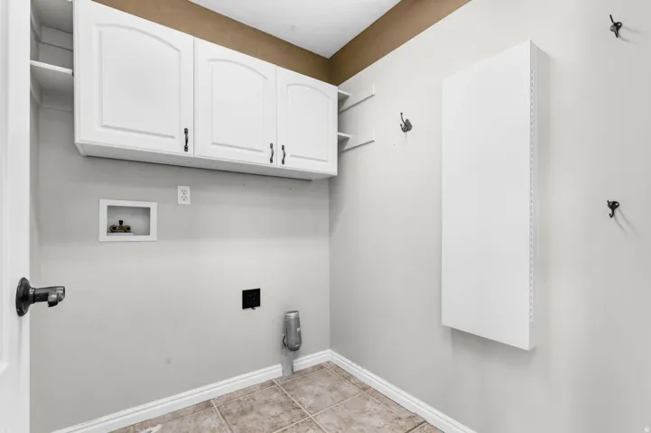 Utility room featuring overhead white cabinetry with arch panel doors and dark hardware, open shelving, and tiled flooring