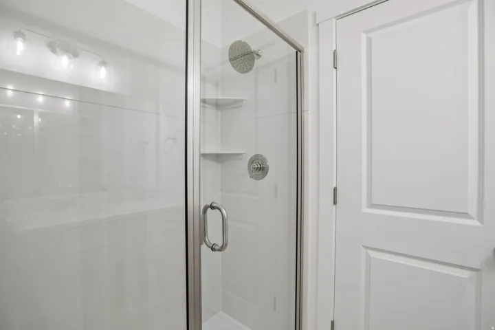 Shower enclosure with glass paneling and chrome hardware, featuring a rain shower head and integrated shelving