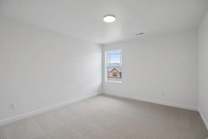 Neutral-toned carpeted room with white walls, a single window, and a flush-mount ceiling light fixture