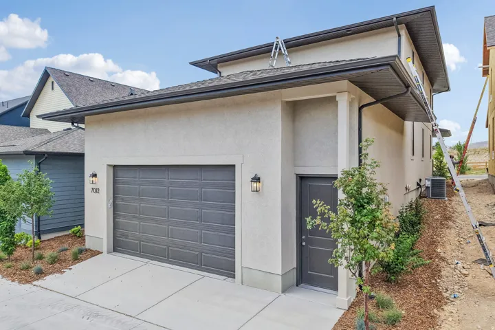 Exterior showcasing a dark gray paneled garage door, a side entry door, and textured stucco siding