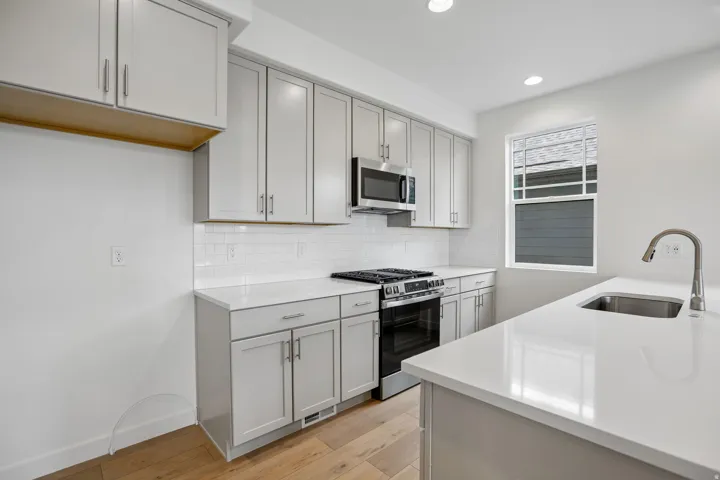 Kitchen featuring light gray cabinetry, white quartz countertops, stainless steel appliances, a subway tile backsplash, and light wood-finish flooring