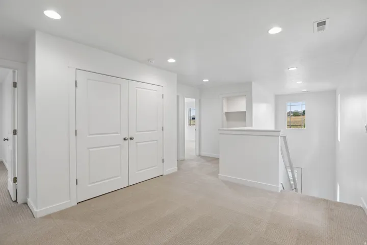 Upper-level landing featuring neutral carpeting, recessed lighting, white panel doors, and a built-in alcove with shelving