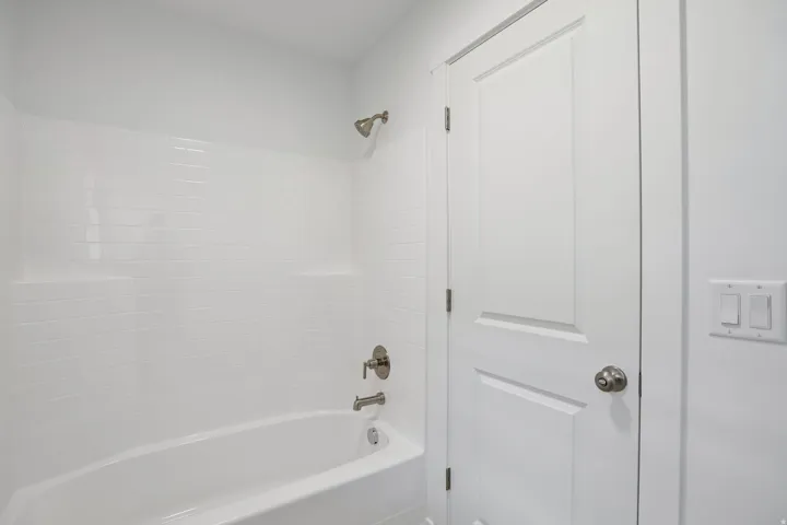 Bathtub and shower combination featuring a white subway tile surround, brushed nickel fixtures, and integrated shelving