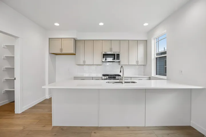 Modern kitchen featuring a large island with an undermount sink, stainless steel appliances, light-toned cabinetry, subway tile backsplash, and wood-finish flooring