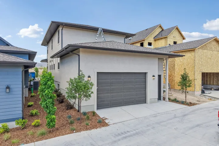 Contemporary stucco exterior with a two-car garage, concrete driveway, and established landscaping