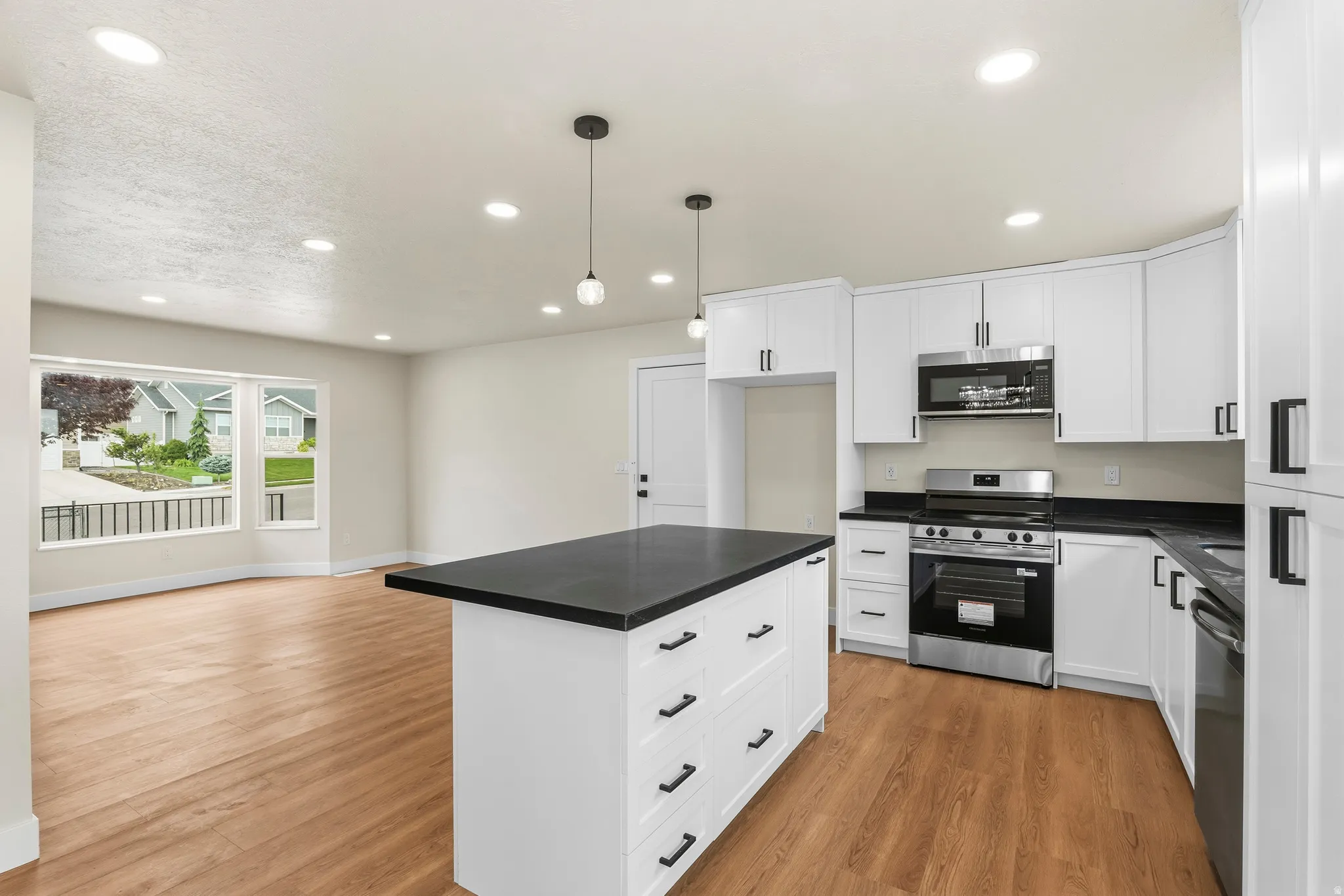 Open-concept kitchen featuring a central island with black countertop, white cabinetry with black hardware, wood-finish flooring, and stainless steel appliances