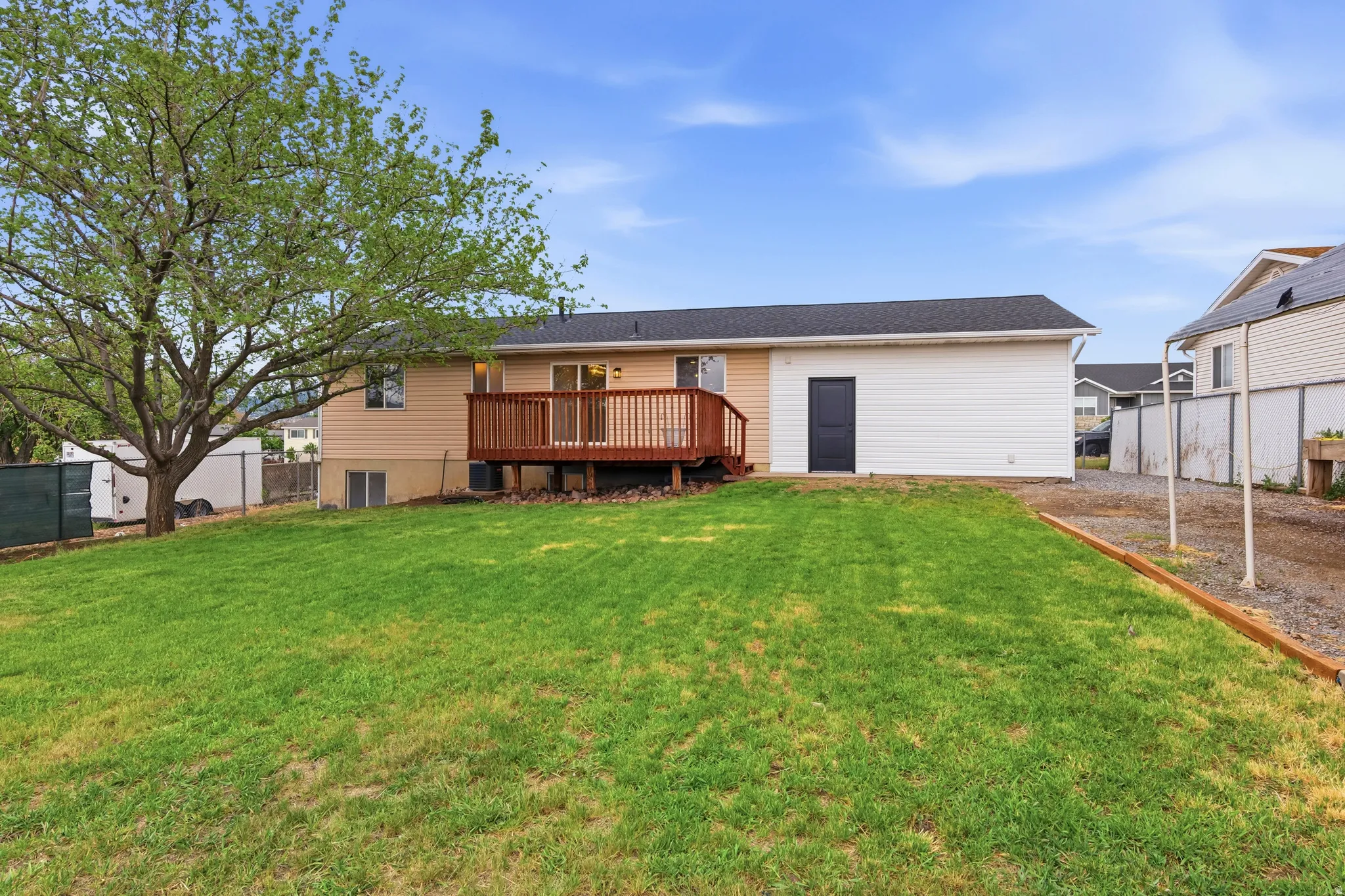 Expansive green lawn with a mature tree, a rear-facing deck featuring wood railing, and a walk-out basement