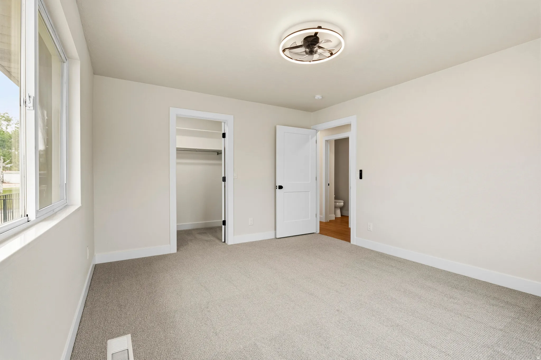 Room featuring light-toned walls, gray carpeting, and a modern ceiling fan with integrated lighting