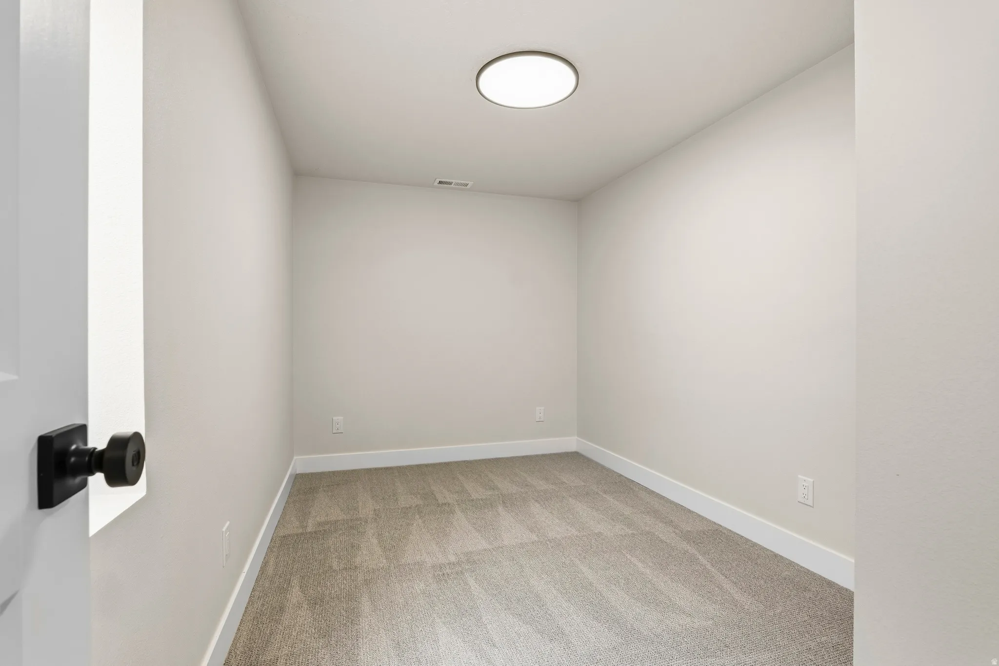 Interior room featuring light-toned walls, grey patterned carpeting, and white baseboards