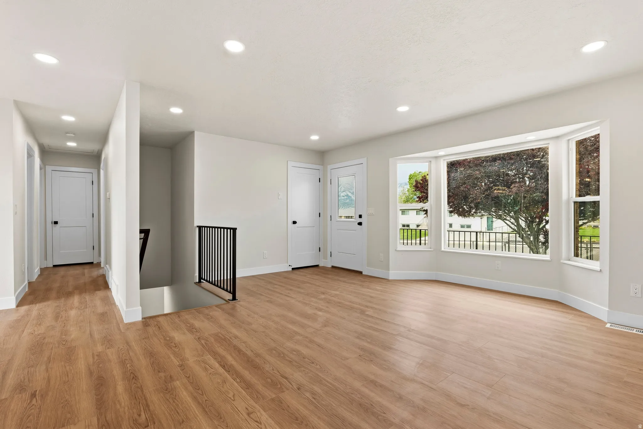 Spacious room featuring wood-finish flooring, recessed lighting, and a prominent bay window