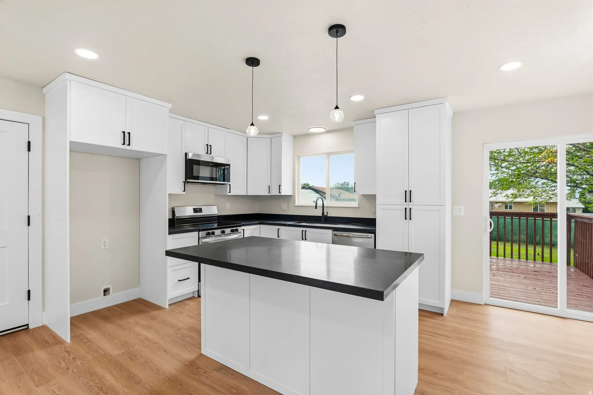 Modern kitchen featuring white shaker cabinetry, dark countertops, stainless steel appliances, and a central island