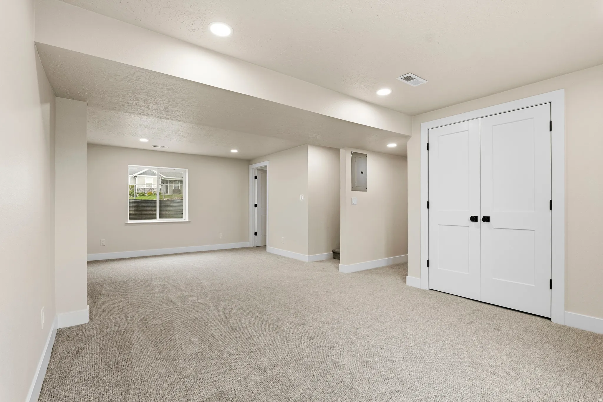 Spacious room featuring neutral carpeting, recessed ceiling lighting, a window providing natural light, and a pair of panel-style double doors with matte black hardware