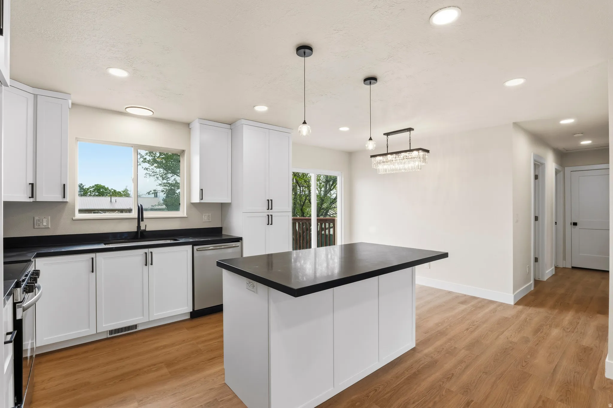 Modern kitchen featuring white shaker cabinetry, black countertops, stainless steel appliances, and wood-finish flooring