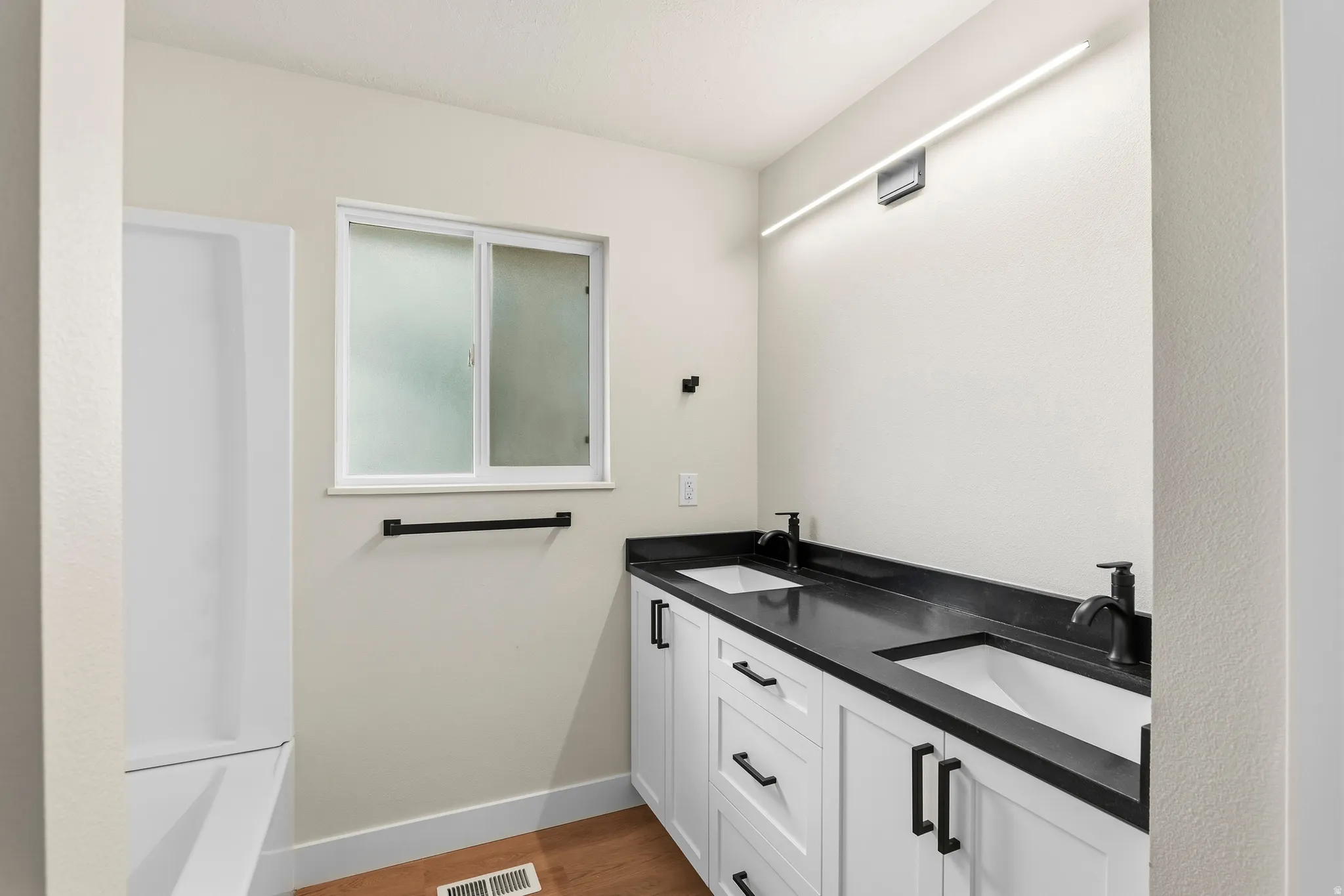 Dual sink vanity with white cabinetry and dark countertops