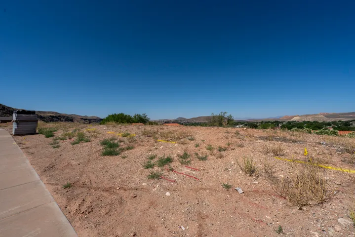 Expansive undeveloped lot featuring a clear building site, a paved sidewalk border, and distant mountain scenery
