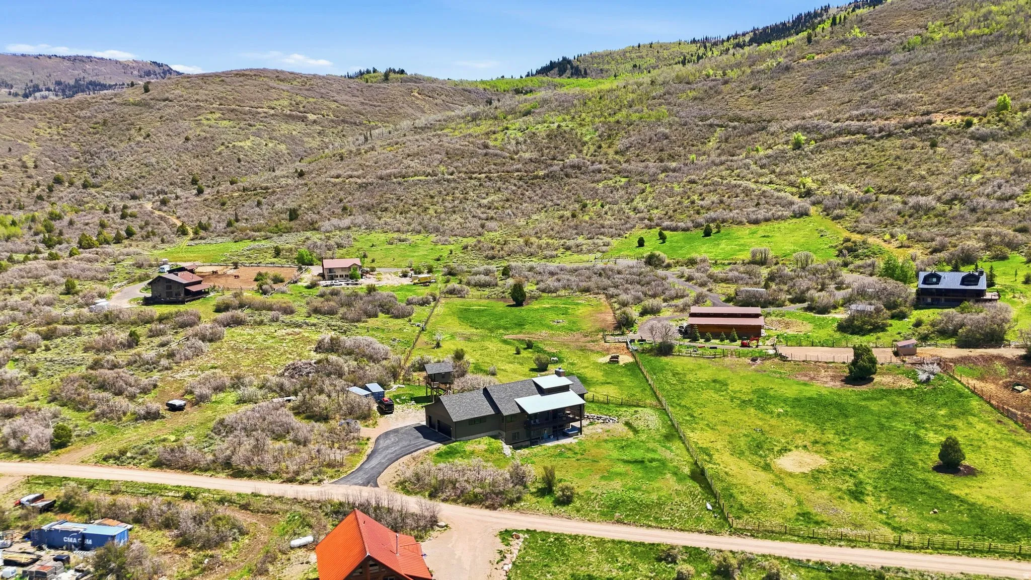 Expansive property featuring multiple structures, verdant green fields, natural brush, and mountainous terrain