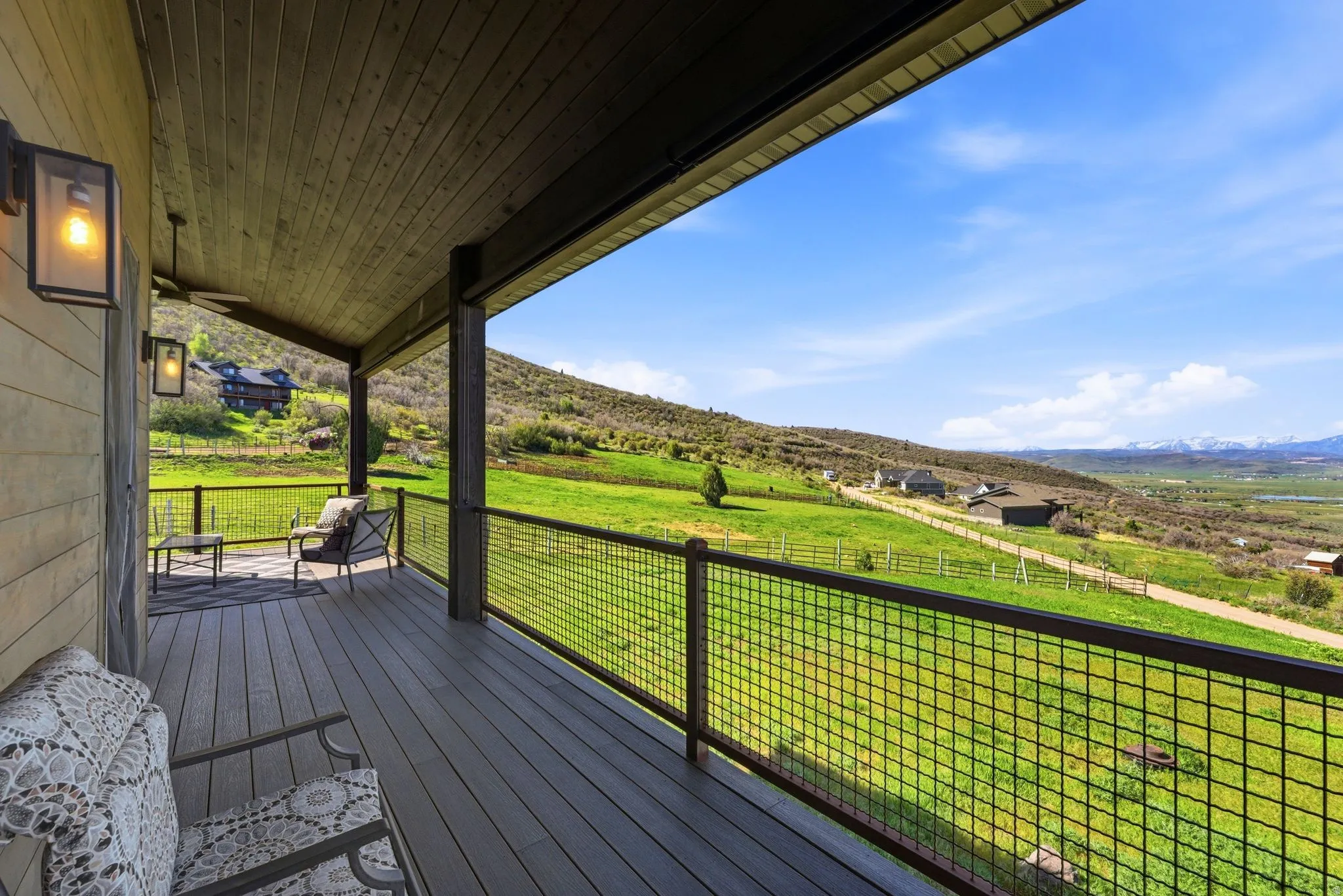 Expansive covered deck featuring composite wood-finish decking, dark wood support columns, and mesh railing