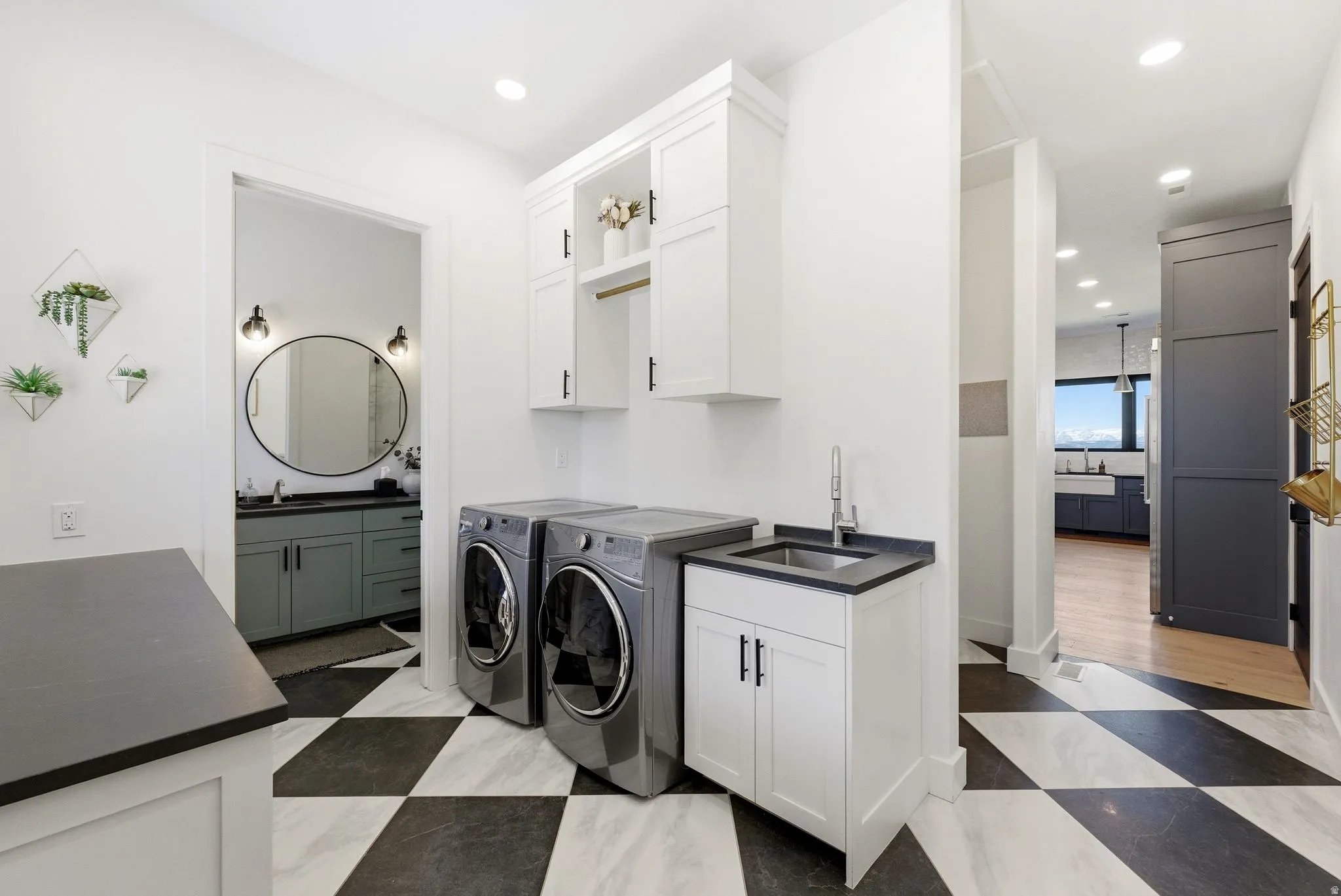 Dedicated laundry area featuring a checkerboard tile floor, built-in white cabinetry, a utility sink with a black countertop, and contemporary front-load appliances