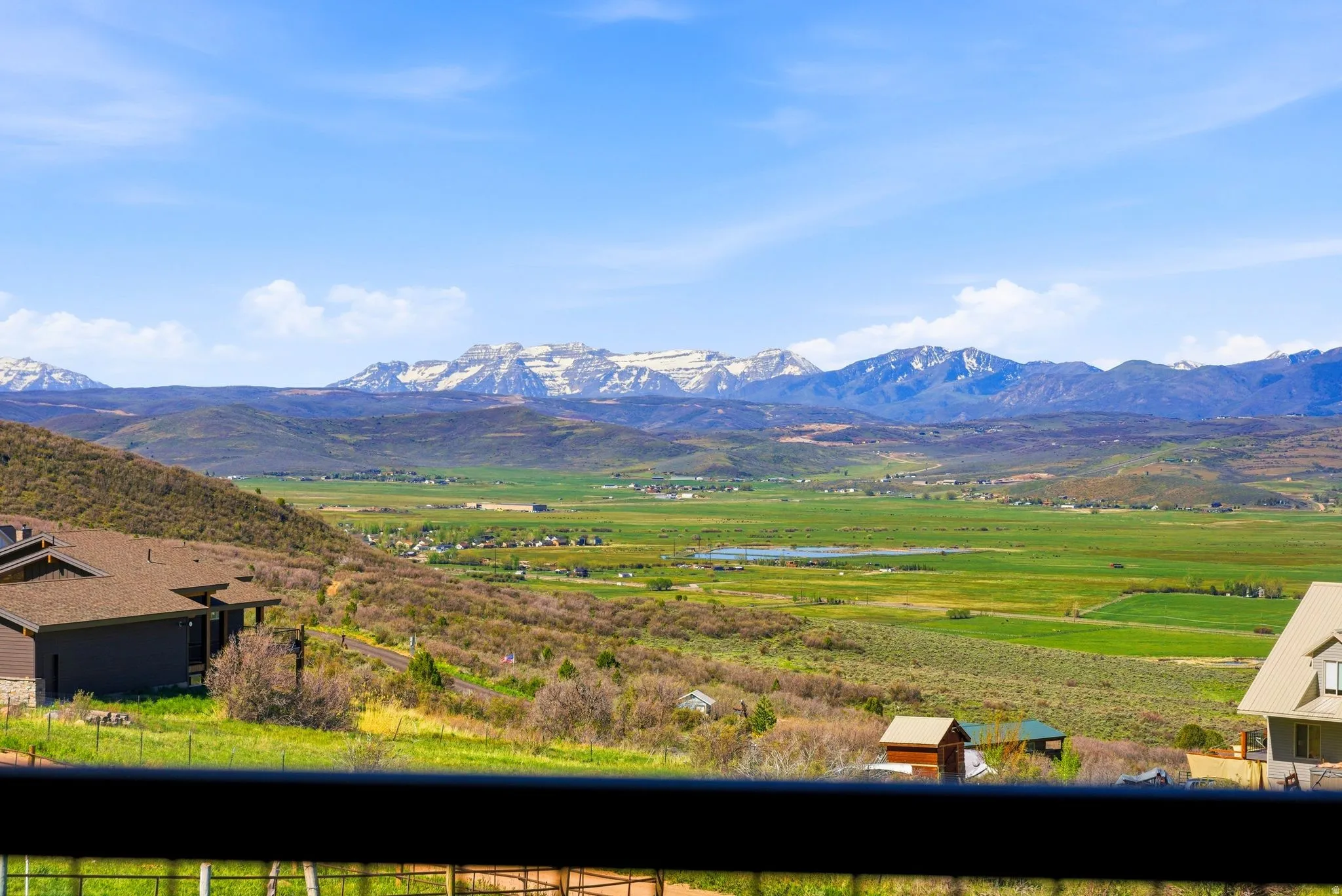 Mountain scenery featuring a broad valley, distant snow-capped peaks, and extensive green landscapes under a clear sky