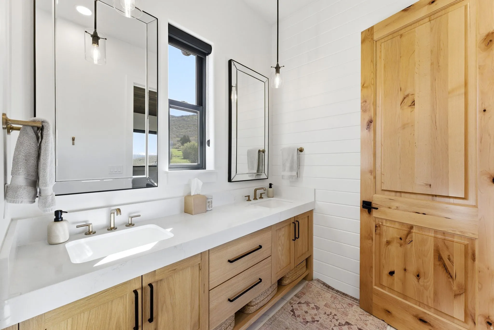 Double vanity with light wood cabinetry, white countertops, and dual undermount sinks