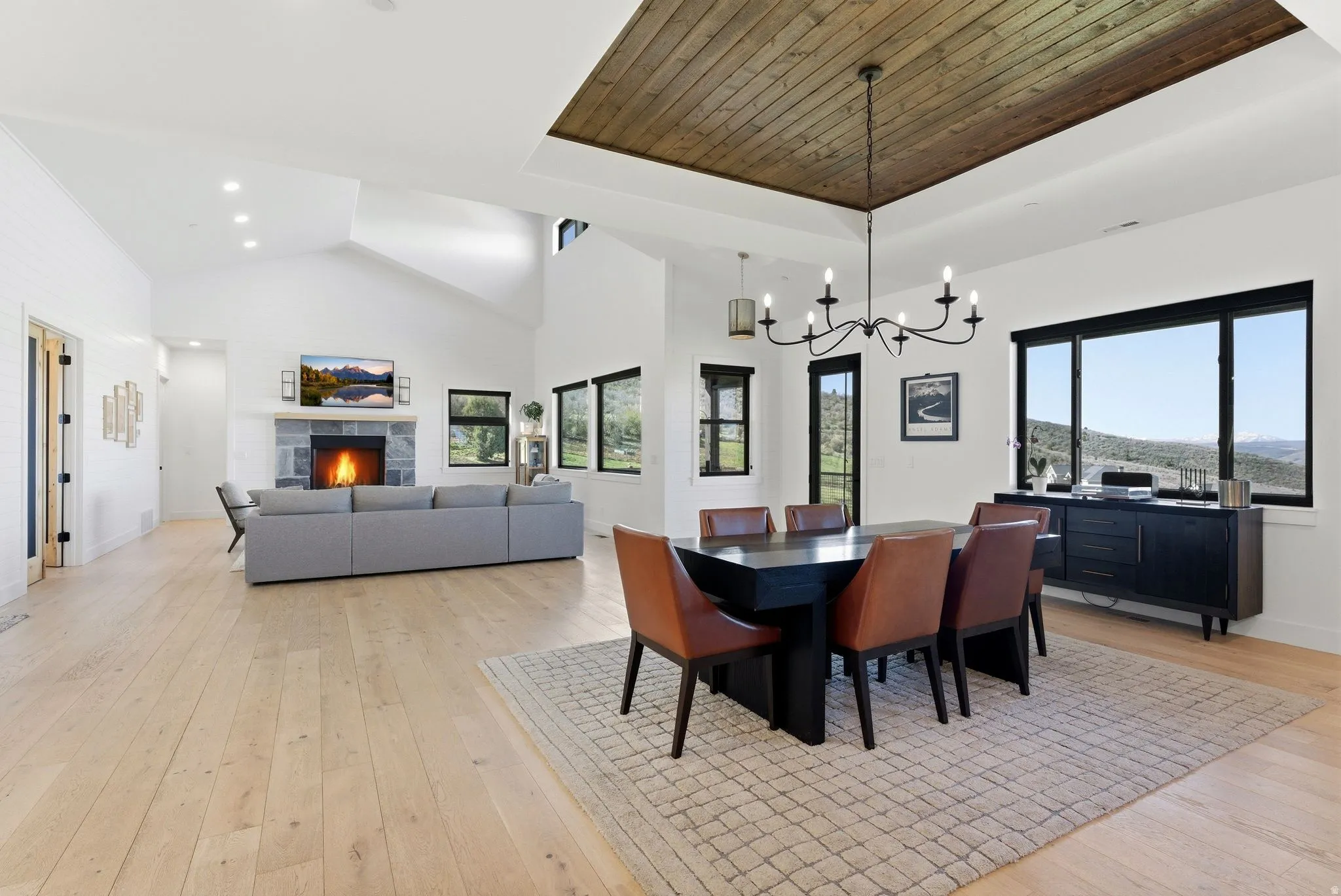 Spacious living area featuring light wood-finish flooring, a stone fireplace with a substantial mantel, and vaulted ceilings with recessed lighting