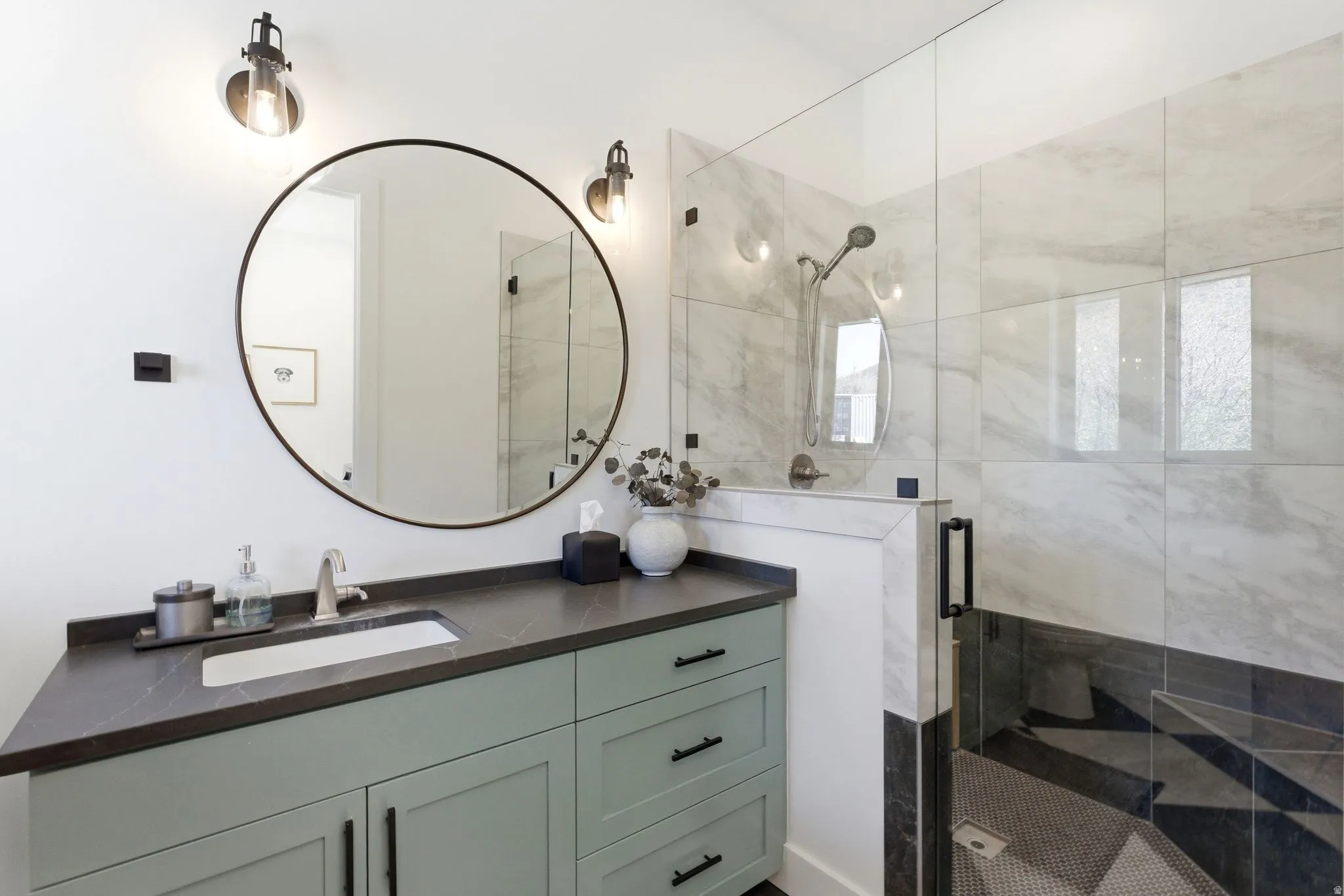 Contemporary bathroom featuring a sage green vanity with dark hardware, a dark countertop, and an undermount sink