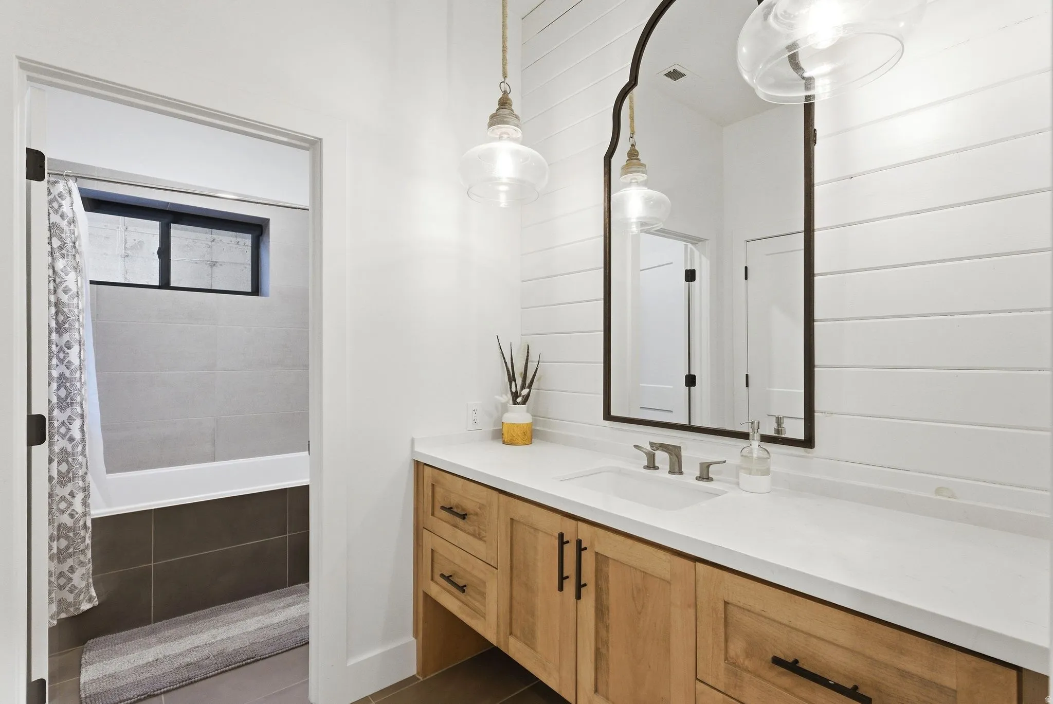 Bathroom vanity featuring a wood-finish cabinet with black hardware, a white countertop, and an undermount sink with a brushed nickel faucet