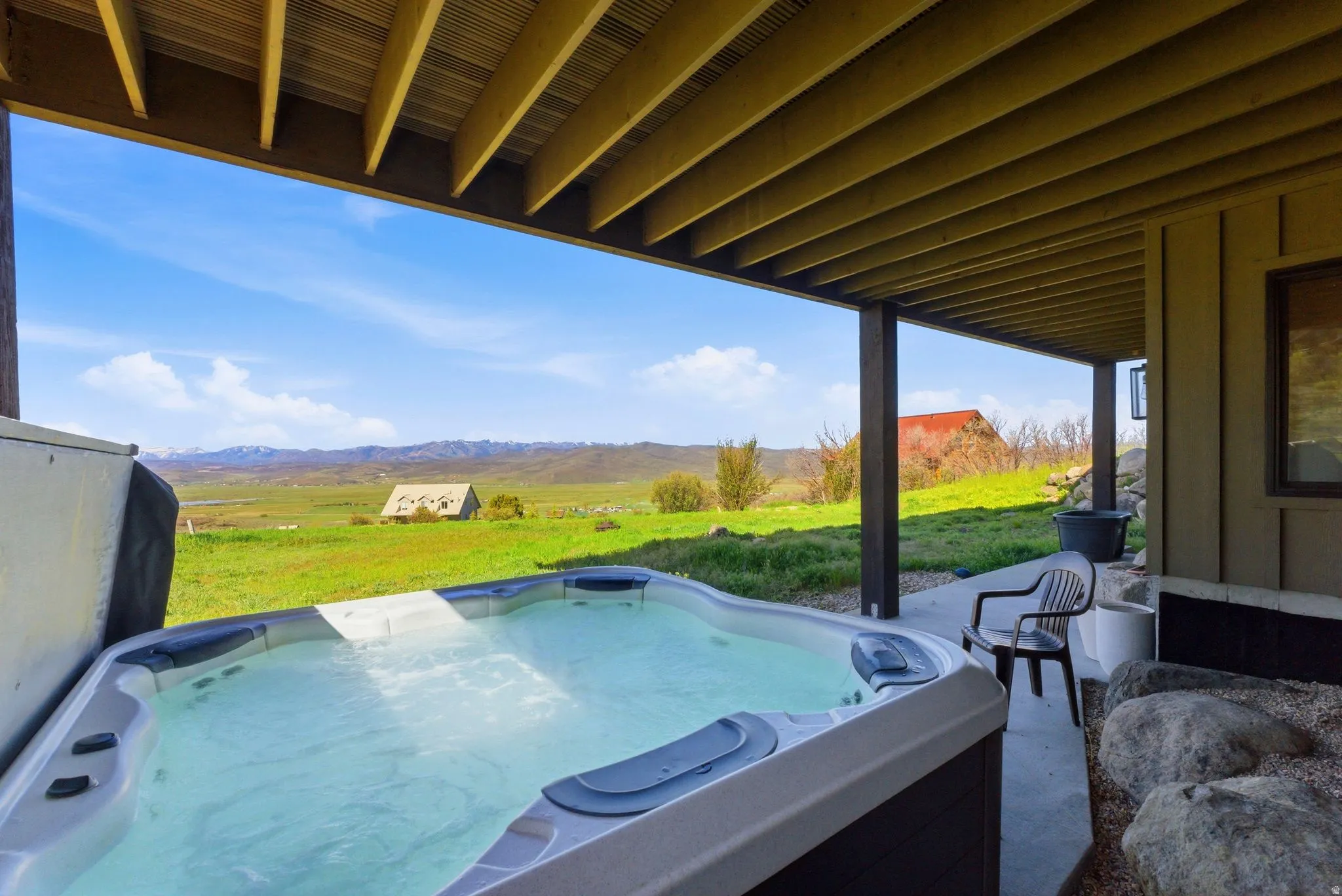 Covered outdoor patio featuring a built-in hot tub, concrete flooring, and an open-beam ceiling