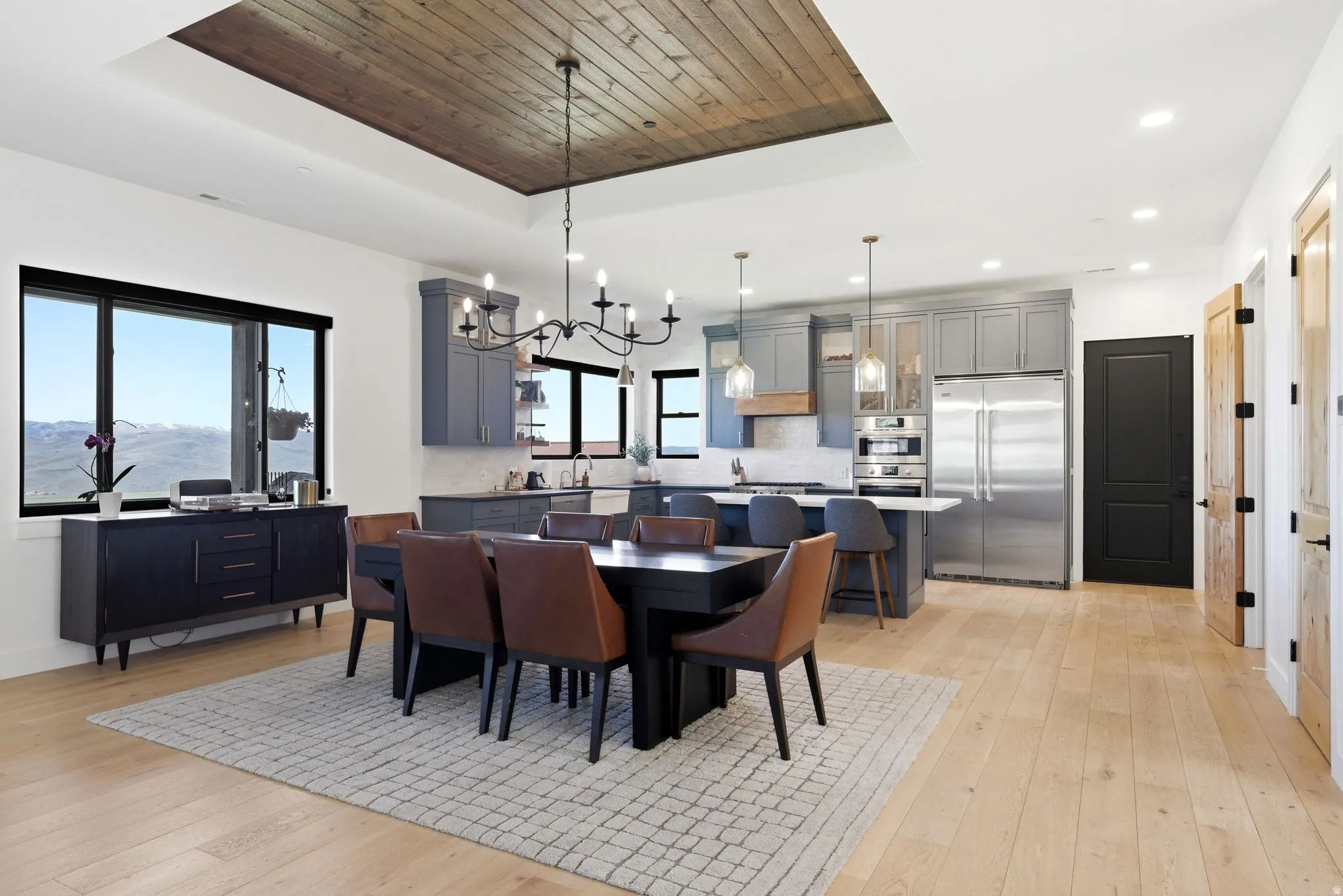 Open-concept living space featuring wood-finish flooring, a recessed ceiling with wood paneling, and a contemporary chandelier