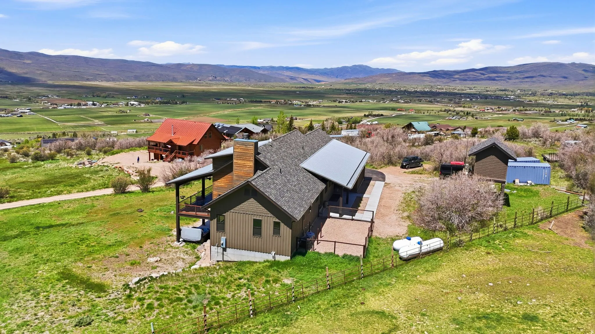 Contemporary residence featuring a pitched roofline, natural wood accents, an outdoor deck, a gravel driveway, and expansive green grounds with mountain scenery