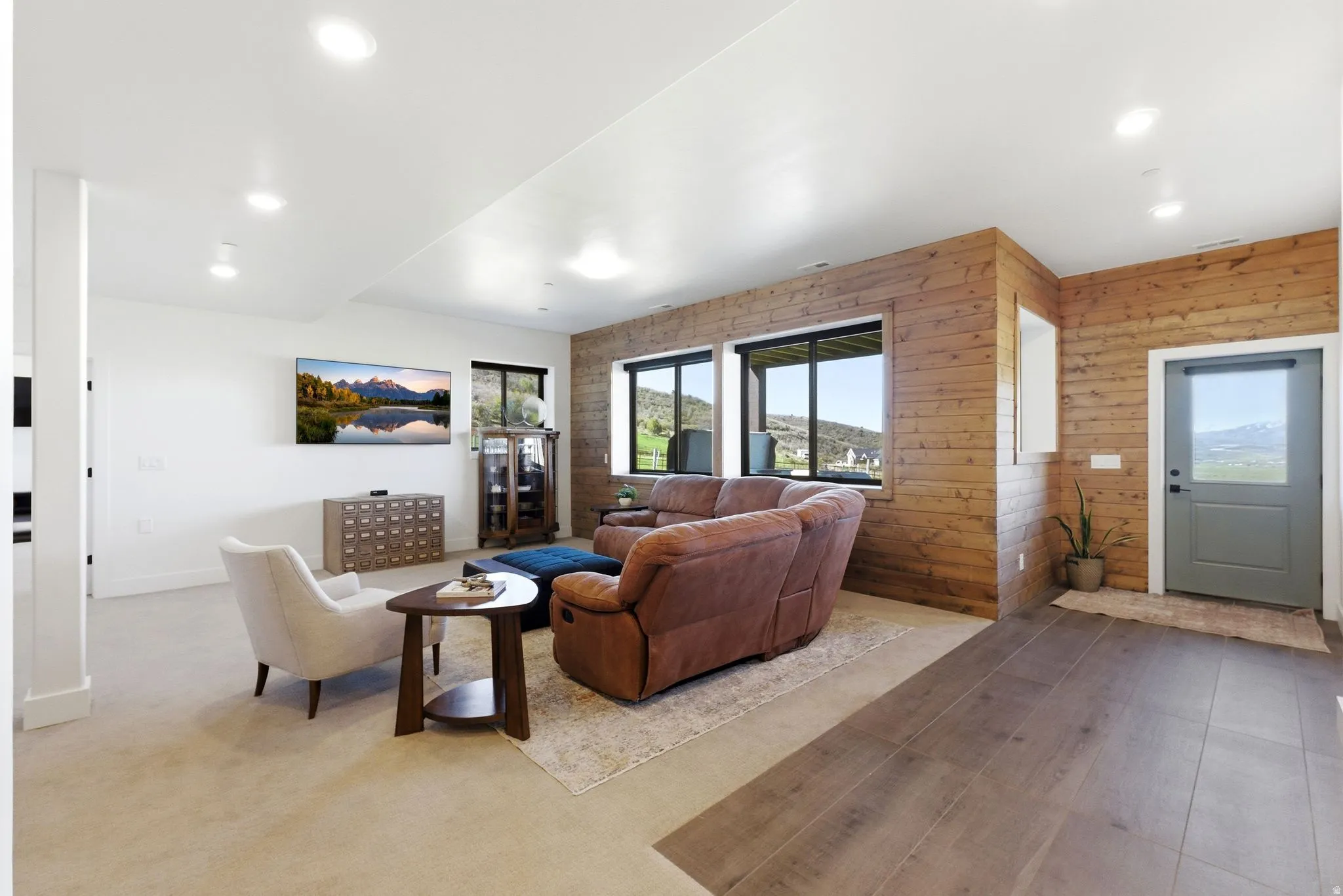 Spacious living area featuring plank wood-finish accent walls, multiple windows, recessed lighting, and a modern gray door with a clear glass panel