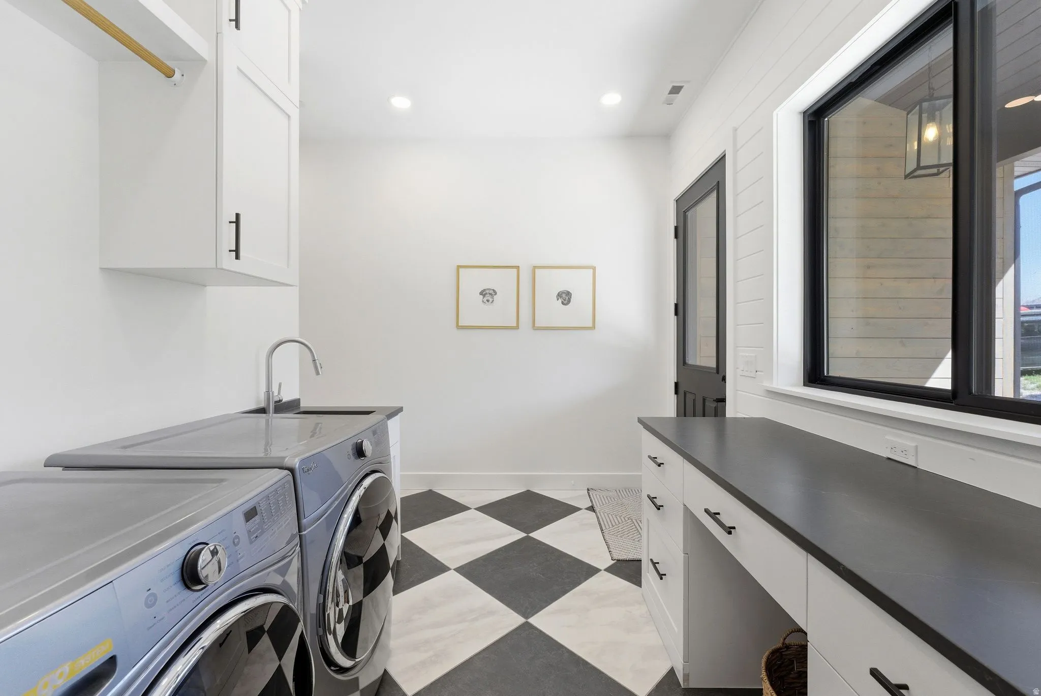 Laundry area featuring black and white checkerboard flooring, a utility sink with a chrome faucet, white cabinetry with black hardware, and a black-framed window