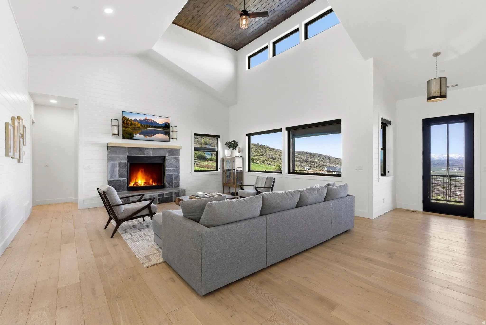 Vaulted ceilings with a dark wood-finish accent panel, a stone-clad fireplace, and expansive windows