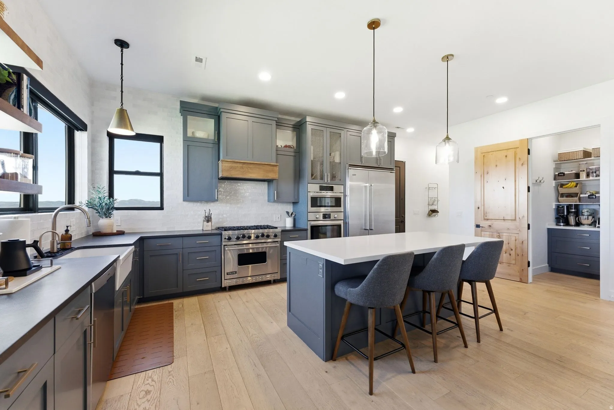 Expansive kitchen featuring a large central island, full suite of stainless steel appliances, grey cabinetry, and light wood-finish flooring
