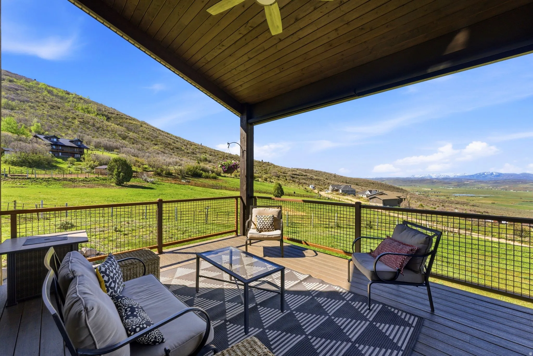 Expansive outdoor patio featuring composite decking, a wood-paneled ceiling with a fan, and a metal grid railing