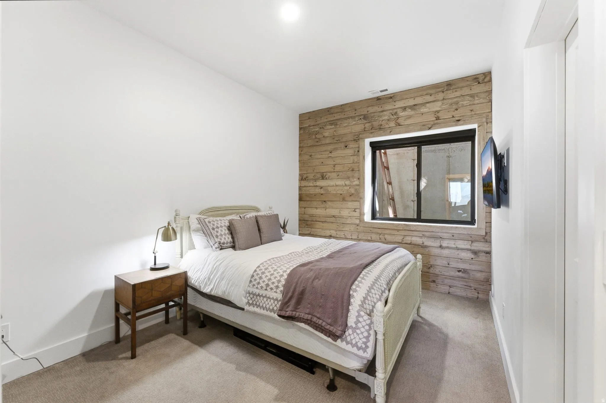 Room featuring a wood-finish accent wall with an integrated window, recessed ceiling lighting, wall-mounted television, and neutral carpet flooring