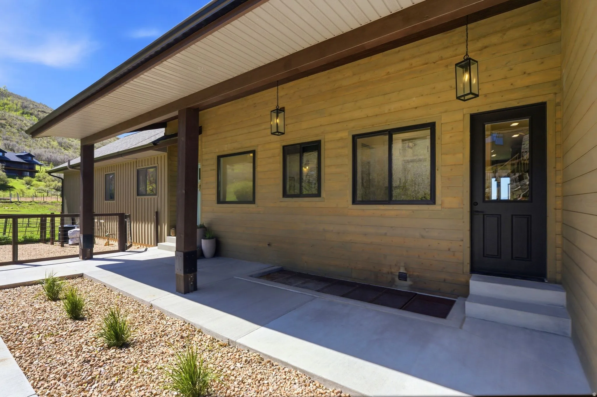 Covered concrete patio with wood-finish siding, dark framed windows, and two hanging lantern-style light fixtures