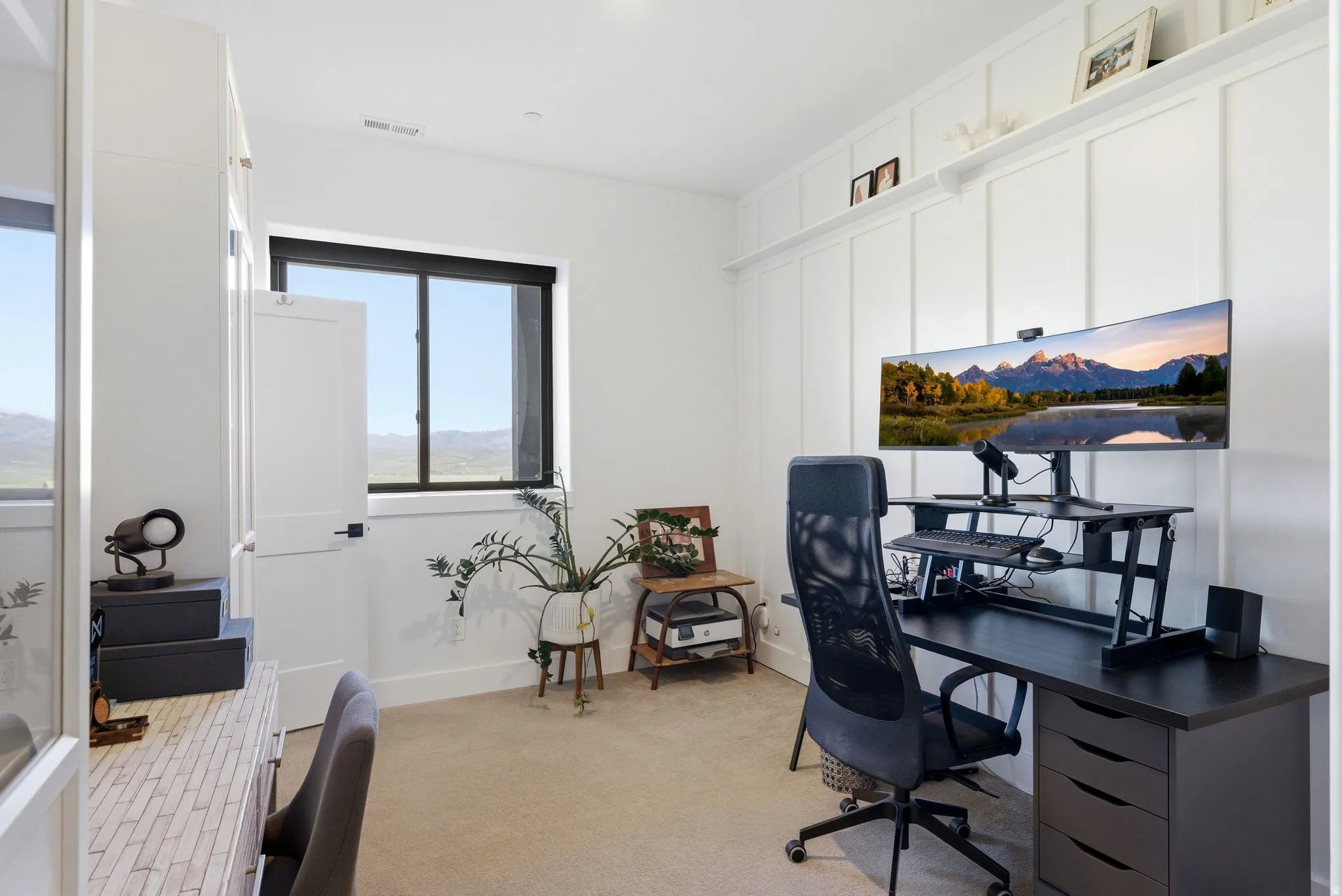 Bright room featuring a large window with black trim, white wall paneling, and carpeted flooring