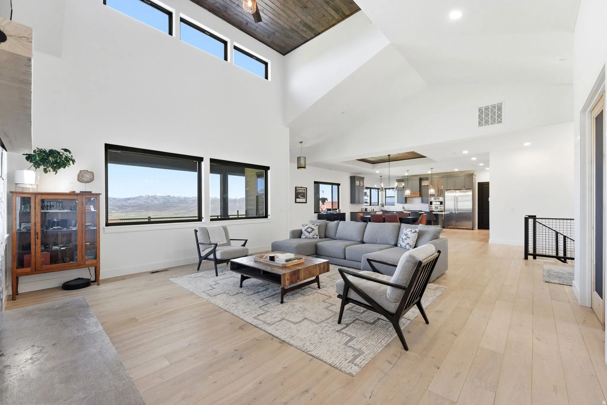 Vaulted ceilings with wood-paneled accents, large picture windows, light wood-finish flooring, and a contemporary open-concept design integrating the kitchen space